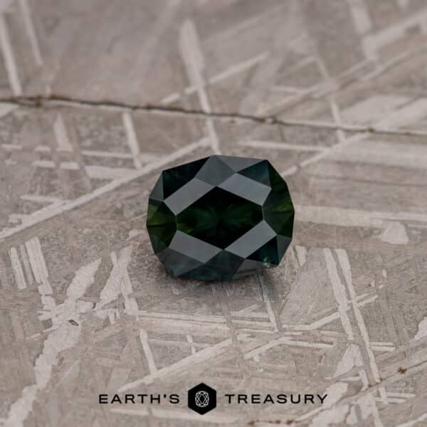 A faceted gemstone, the 3.02-Carat Deep Blue-Green Particolored Australian Sapphire, sits on a background with a geometric pattern. The sapphire showcases a deep, rich blue-green color and multiple facets that give it a brilliant shine. The text "EARTH'S TREASURY" is printed at the bottom of the image.