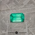 A vibrant, rectangular-cut 2.13-carat bright green emerald is showcased on a textured gray surface. The imagery features the brand logo "EARTH'S TREASURY" at the bottom. The emerald displays a rich green hue with visible internal characteristics typical of natural stones.