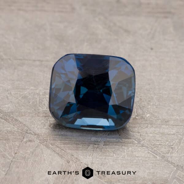 A 2.14-carat Robin's Egg Blue Montana Sapphire with a cushion cut and faceted surface sits on a textured, light-colored background. The text "EARTH'S TREASURY" is at the bottom center of the image.