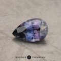 A 3.10-carat bluish violet to purple color-change sapphire, expertly cut into a pear shape, rests gracefully on a textured gray surface. The gem's facets glimmer with light, highlighting its exceptional clarity and detailed craftsmanship. At the bottom of the image is the label "Earth's Treasury.