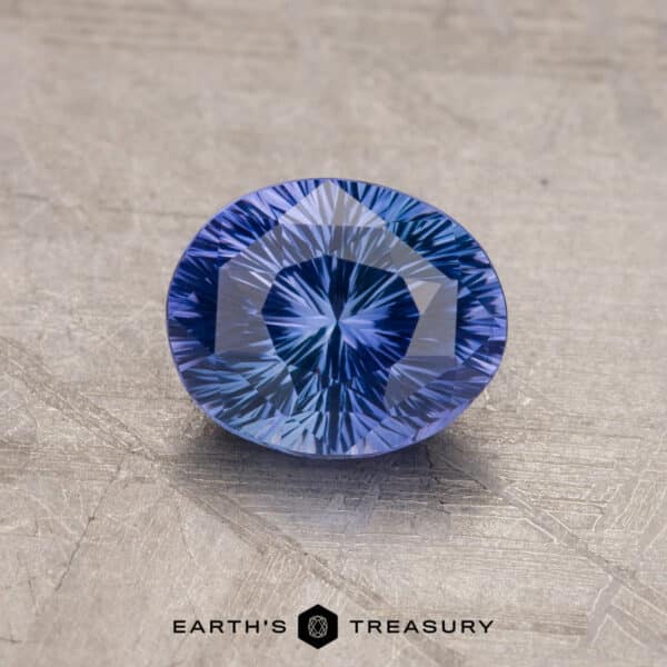 Close-up image of a beautifully cut, 1.53-Carat Royal Blue Ceylon Sapphire (Heated) with a vivid blue color, displayed on a textured gray surface. The gemstone exhibits a starburst pattern when viewed from above. The words "Earth's Treasury" are visible at the bottom.