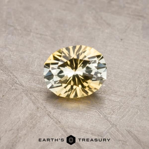 A round, faceted 1.53-carat Royal Blue Ceylon Sapphire (heated) is placed on a rough, textured surface. The background features subtle metallic tones. The logo "EARTH'S TREASURY" and a hexagonal emblem are visible at the bottom.