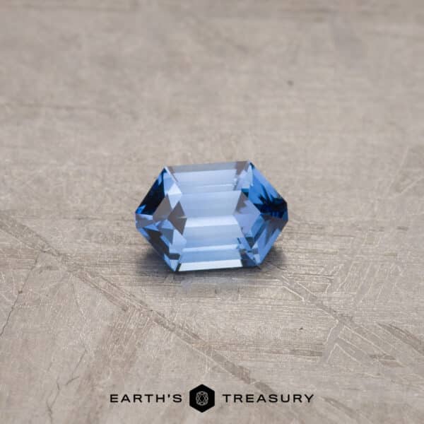 A 1.53-carat Royal Blue Ceylon Sapphire (heated) rests on a textured gray surface. The background has a rough, scratched appearance. The text "Earth's Treasury" is printed below the gemstone.