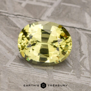 A faceted, oval-cut 1.78-carat Mali Garnet, placed on a textured gray surface, with the logo and text "Earth's Treasury" visible at the bottom.