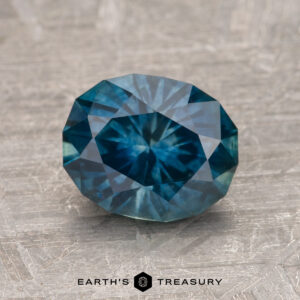 A 1.93-carat Montana sapphire (heated), featuring a faceted blue gemstone with a star-like pattern at its center, displayed on a textured surface. The label "Earth's Treasury" is present at the bottom of the image.