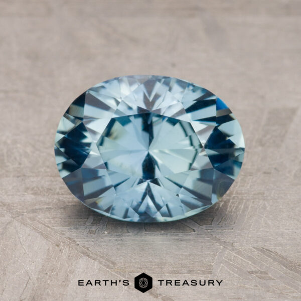 A 2.21-carat Ceylon sapphire with a bluish hue is displayed on a textured surface, with the text "Earth's Treasury" visible below the gemstone.