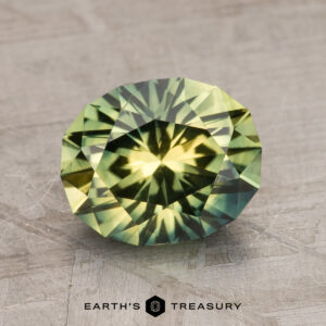 A round, multi-faceted 2.65-carat Australian Sapphire, displaying vibrant green and yellow hues, is showcased on a textured surface. The text below reads "Earth's Treasury.