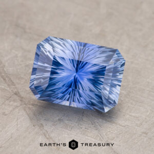 A 2.23-carat, rectangular blue sapphire from Ceylon with intricate starburst-like patterning, labeled "Earth's Treasury" on a textured surface.