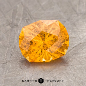 A faceted orange gemstone on a textured grey surface with a label that reads "ET1146" at the bottom.