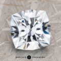 A close-up photo of the polished, cushion-cut 4.23-Carat Pale Aqua Montana Sapphire, featuring a "Earth's Treasury" logo at the bottom center. The gem exhibits a stunning array of sparkling facets against a textured surface background.