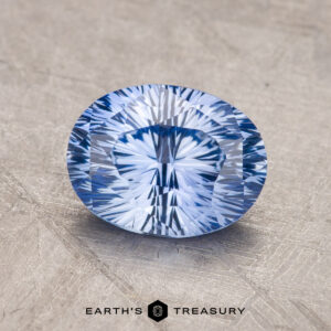 A 1.83-carat Ceylon sapphire, with an oval-shaped and faceted cut, rests on a textured surface with the words "Earth's Treasury" beneath it.