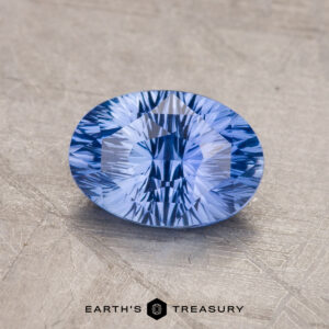 A faceted blue 1.82-carat Ceylon Sapphire is displayed on a gray surface, with the text "Earth's Treasury" and its logo visible at the bottom.