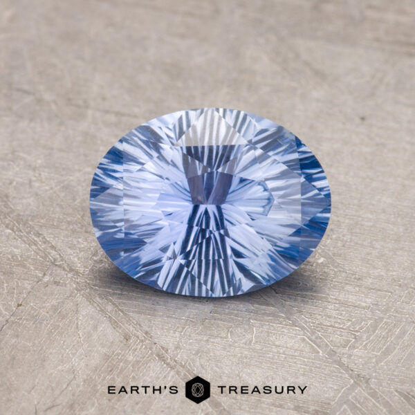 A faceted oval-cut blue 1.38-Carat Ceylon Sapphire displayed on a textured surface with the text "EARTH'S TREASURY" at the bottom.