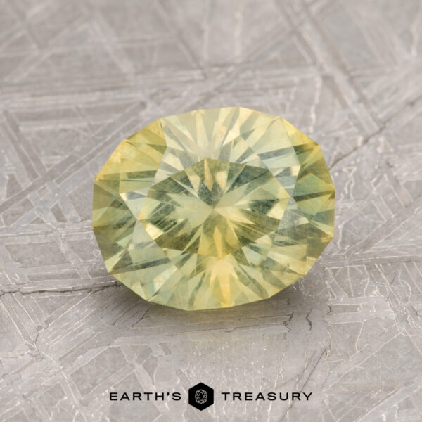 A faceted yellow 2.11-Carat Montana Sapphire displayed on a textured surface with the words "Earth's Treasury" beneath it.