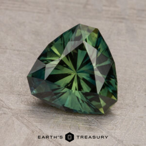 A faceted, green, triangular 2.29-carat Australian Sapphire displayed on a textured gray surface with the Earth's Treasury logo visible at the bottom.