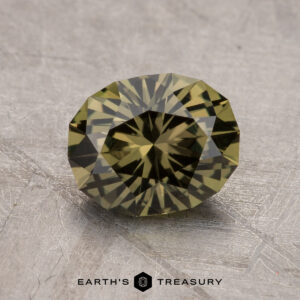 A 1.94-carat round, faceted Australian sapphire with a vibrant green hue is displayed on a textured gray surface, with the text "EARTH'S TREASURY" visible at the bottom of the image.