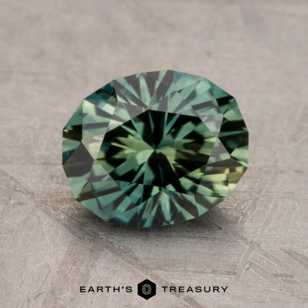 A 2.47-carat round-cut Australian Sapphire with intricate facets is displayed on a textured surface. The bottom of the image features the text "EARTH'S TREASURY" alongside a small logo.