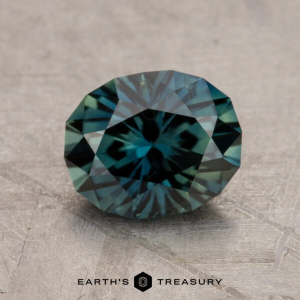 A 2.10-carat Australian sapphire with dark green and blue hues placed on a textured surface. The text "EARTH'S TREASURY" is visible at the bottom of the image.