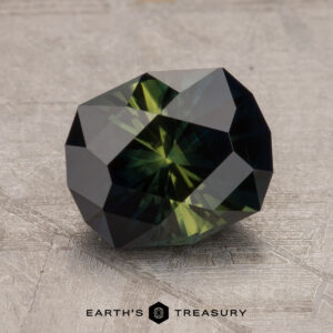 A 2.51-carat Australian Sapphire, faceted with a hexagonal shape and displaying a dark green hue, is showcased on a textured, light-colored surface. Text at the bottom reads "Earth's Treasury.