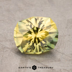 A 2.43-carat Australian sapphire with a yellow-green hue is displayed on a flat, plain surface. The Earth's Treasury logo is visible at the bottom of the image.