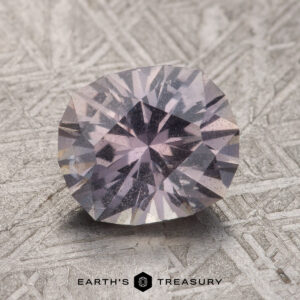 A faceted 2.34-carat gemstone that shifts from pale gray-lavender to pink-purple rests on a textured metallic surface, with the text "Earth's Treasury" inscribed below it.