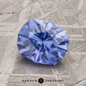 A 2.00-Carat Violet-Blue Umba Sapphire placed on a textured grey surface, with the "Earth's Treasury" logo at the bottom center.