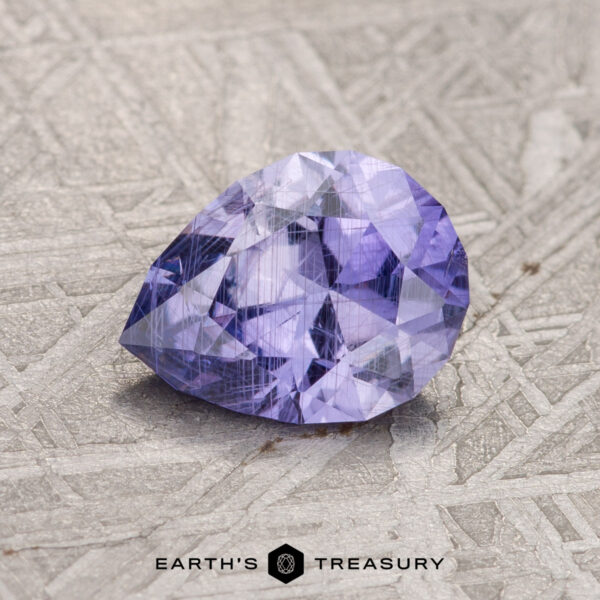 A 1.34-carat, pear-shaped faceted Purple Umba Sapphire lies on a textured surface. The words "Earth's Treasury" are written at the bottom center of the image.