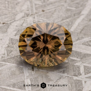 A 2.20-carat warm brown Umba Sapphire is displayed against a textured background. The image text reads "Earth's Treasury.