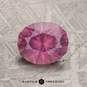 A 2.01-carat Hazy Magenta Umba Sapphire is placed on a textured metallic surface, with the text "EARTH'S TREASURY" visible at the bottom of the image.