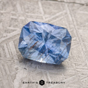 A 2.19-carat medium blue Umba sapphire is displayed on a textured gray surface with the words "Earth's Treasury" below.