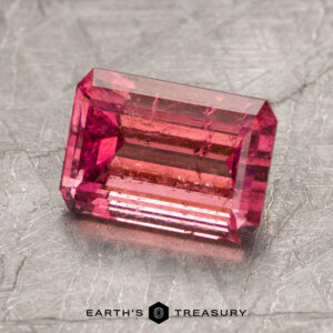 A rectangular pink gemstone, identified as ET1382, is displayed on a textured surface with the words "EARTH'S TREASURY" below it.