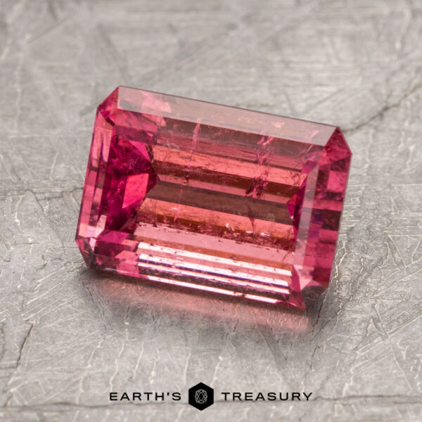 A rectangular pink gemstone, identified as ET1382, is displayed on a textured surface with the words "EARTH'S TREASURY" below it.