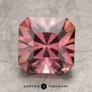 Square-cut pink gemstone labeled "ET1357" at the bottom. The stone is placed on a textured gray surface.