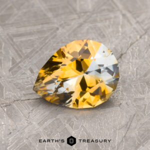 A faceted, pear-shaped gemstone with gradients of yellow and clear hues, set on a textured surface with "1.26-Carat Montana Sapphire (Heated)" text below it.