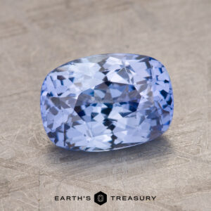 The 2.09-Carat Celyon Sapphire, a faceted, rectangular light blue gemstone with intricate internal reflections, is placed on a textured gray background.