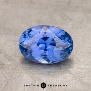 A 1.83-carat oval-cut Ceylon sapphire, featuring intricate facets, is showcased against a textured background. Text at the bottom center of the image reads "EARTH'S TREASURY.