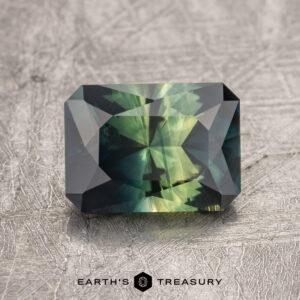 A 2.05-carat Australian sapphire with rectangular cut and geometric facets rests on a textured surface, with the logo "Earth's Treasury" displayed beneath it.