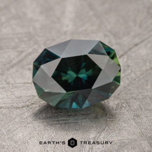 A faceted, multicolored 1.94-carat Australian Sapphire with a hexagonal pattern at its center is displayed on a textured surface with the label 'Earth's Treasury' below it.