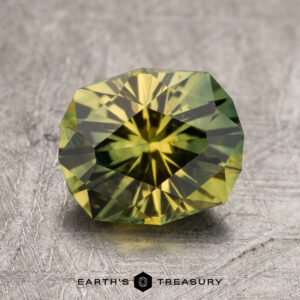 A 2.36-carat Australian sapphire, with a green-yellow hue and complex internal patterns, is displayed on a textured surface. The faceted gemstone boasts a striking hexagonal shape. Below the gem, the text "Earth's Treasury" is prominently visible.