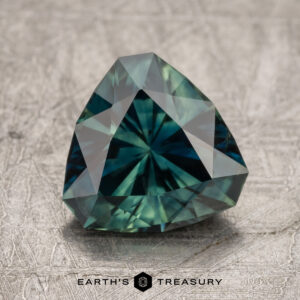 A faceted, trilliant-cut 2.44-carat Australian sapphire gemstone positioned on a textured surface. The stone is displayed with the logo "Earth's Treasury" beneath it.