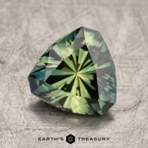 A 2.36-carat Australian sapphire in a trilliant cut with intricate facets, showcased on a textured surface. Text at the bottom reads "EARTH'S TREASURY.