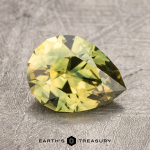 A cut, yellow-green gemstone, specifically a 1.61-Carat Australian Sapphire, is displayed on a textured surface. Text below reads "EARTH'S TREASURY.