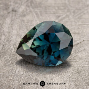 A faceted 1.61-carat Australian Sapphire with enchanting hues of blue and green rests on a textured surface, with the logo "EARTH'S TREASURY" visible at the bottom of the image.