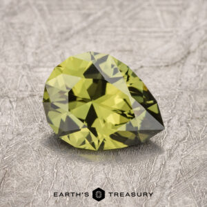 A 1.47-carat Australian sapphire, displaying a stunning faceted yellow-green hue, rests on a textured surface with the text "EARTH'S TREASURY" below it.