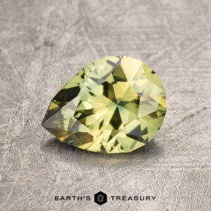 A 1.40-carat Australian Sapphire, cut in a pear shape and faceted in a brilliant green hue, is displayed on a textured, gray surface. The text "EARTH'S TREASURY" appears at the bottom center of the image.