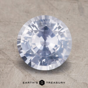 A close-up image of a faceted 3.06-Carat Sapphire, its blue hue glistening on a textured surface. At the bottom, the text reads "EARTH'S TREASURY.