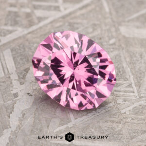 A 2.02-carat Bubblegum Pink Mahenge Garnet displayed on a textured surface with the logo and text "Earth's Treasury" below.