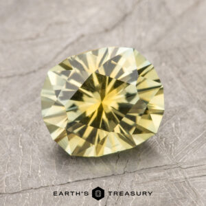 Close-up of a faceted, oval-shaped yellow 2.19-Carat Montana Sapphire (Heated) on a textured gray surface. The logo "Earth's Treasury" is visible at the bottom.