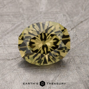 A round, yellow gemstone with intricate faceting, resting on a textured silver surface. Caption on the image reads "1.96-Carat Australian Sapphire from EARTH'S TREASURY.