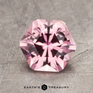 A gemstone, identified as ET1593, features a pink hue and a hexagonal cut, resting on a textured surface with the text "Earth's Treasury" beneath it.